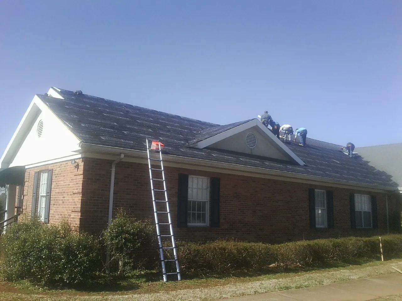 Crew tearing shingles off a brick ranch roof with a ladder set — Metal Roof Repair work by our crew in Shannon