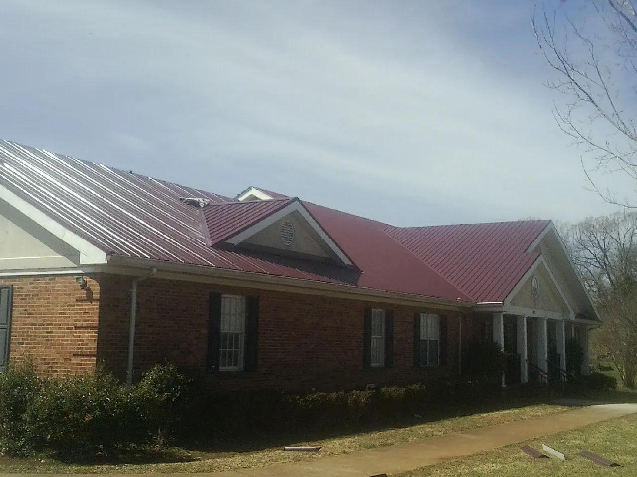 Red metal roof with gabled entries on a long brick building, from a Hail Damage Roof Repair job in Shannon