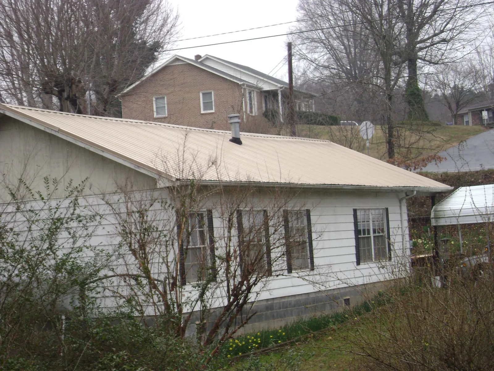 Tan metal roof on a white sided house set into a hillside — Commercial Roofing by Roofing Brothers in Shannon