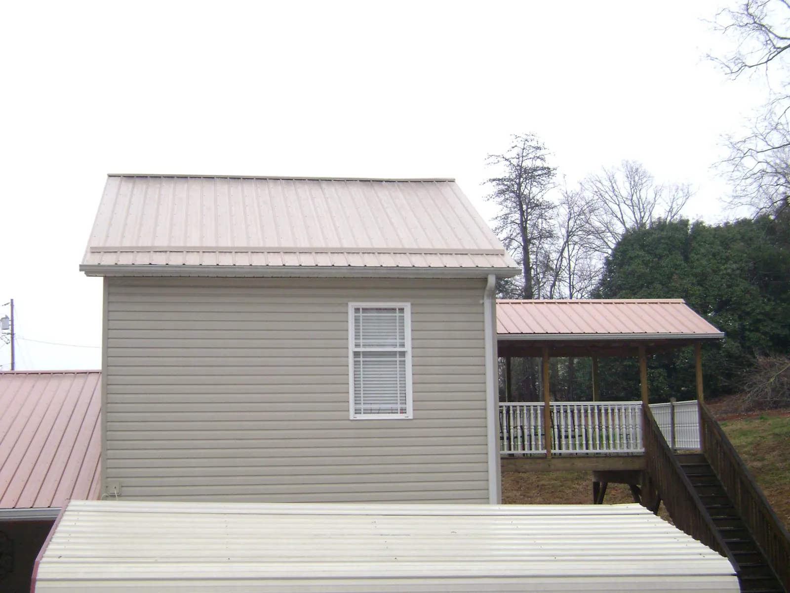 Tan metal roofs on a two story addition and attached porch, from a Roof Replacement job in Shannon